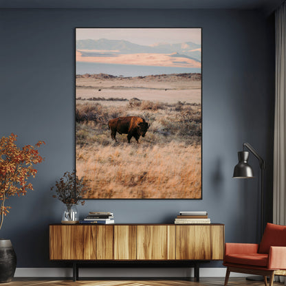A solitary bison standing in golden prairie grass with distant mountains and soft sunset light, ideal for rustic, lodge, and western decor.