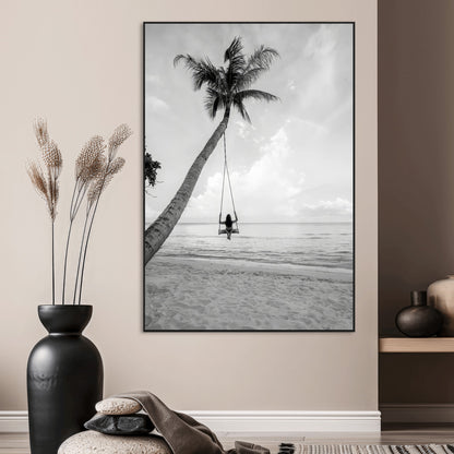 Monochrome photo of a woman swinging from a palm tree on a serene beach, ideal for minimalist or tropical coastal decor.