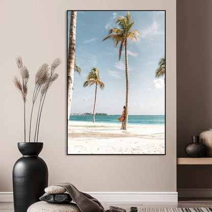 Person leaning on a palm tree at a tropical beach with white sand and turquoise water, perfect for coastal or beach-themed home decor.