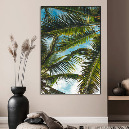 Looking up at lush green palm leaves against a bright blue sky, creating a tropical and relaxing coastal aesthetic.