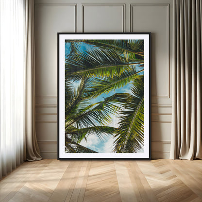Looking up at lush green palm leaves against a bright blue sky, creating a tropical and relaxing coastal aesthetic.