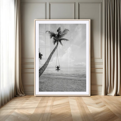 Monochrome photo of a woman swinging from a palm tree on a serene beach, ideal for minimalist or tropical coastal decor.