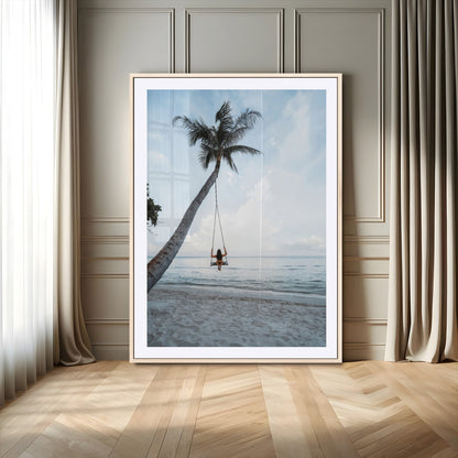 Wall art of a girl on a swing hanging from a palm tree over calm ocean waters, perfect for tropical or minimalist coastal decor.