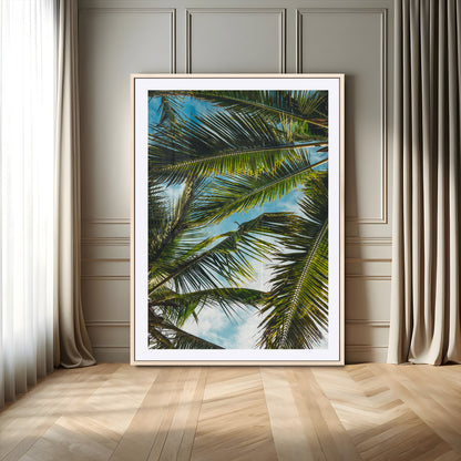Looking up at lush green palm leaves against a bright blue sky, creating a tropical and relaxing coastal aesthetic.