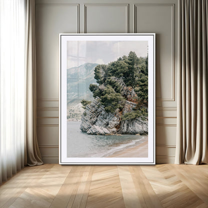 Framed photo of a rocky coastal cliff with dense greenery and calm shoreline, ideal for rustic coastal or earthy-toned home decor.