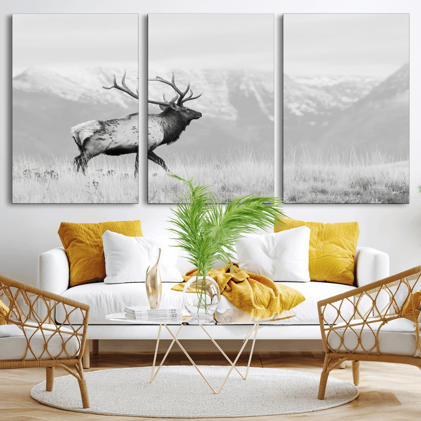 Black and white photograph of a majestic elk standing in a grassy field with snow-capped mountains in the background, creating a bold and rustic wilderness scene.
