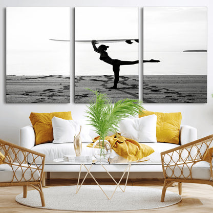 A woman balances a surfboard on her head while striking a yoga pose on the beach, silhouetted against a calm ocean horizon.