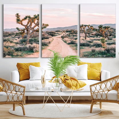 A dusty road winding through Joshua Tree National Park, framed by iconic twisted trees and warm desert tones under a soft pastel sky.
