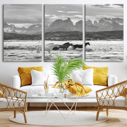A black and white landscape of wild horses grazing in a vast grassland with towering mountains in the background, creating a moody and rustic western aesthetic.