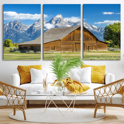 A rustic wooden barn sits in front of towering mountain peaks under a clear blue sky, perfect for farmhouse or cabin style interiors.