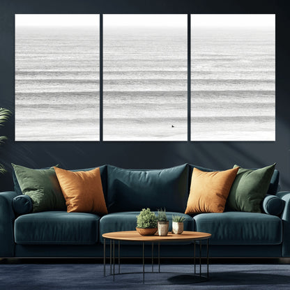 Monochrome photo of a lone surfer in calm layered waves, perfect for minimalist coastal or moody ocean-inspired wall decoration.