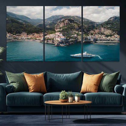 Aerial view of Amalfi Coast, Italy, with colorful hillside houses, lush green mountains, and a luxury yacht sailing in turquoise waters.