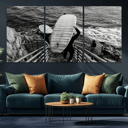 Black and white photo of surfers carrying boards down a rugged cliffside stairway, capturing a bold and adventurous coastal scene.