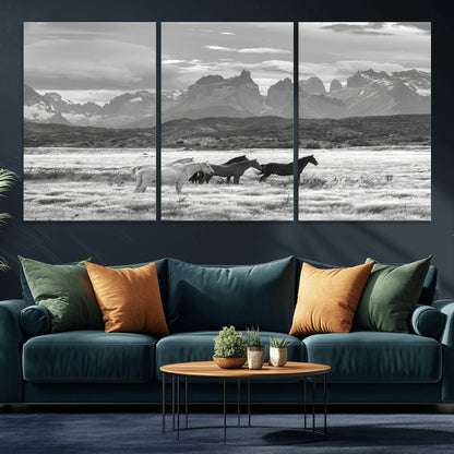 A black and white landscape of wild horses grazing in a vast grassland with towering mountains in the background, creating a moody and rustic western aesthetic.