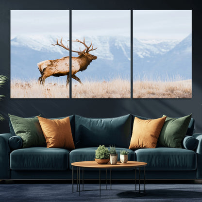 An elk walking on snowy grassland with majestic mountains in the background, ideal for rustic lodge or cabin wall decor.