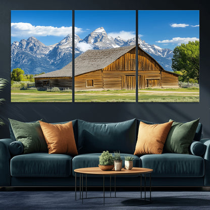 A rustic wooden barn sits in front of towering mountain peaks under a clear blue sky, perfect for farmhouse or cabin style interiors.
