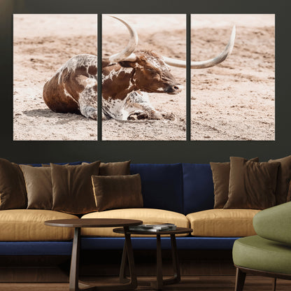 Texas Longhorn bull resting on dusty ground with warm tones, ideal for rustic western or farmhouse-themed wall decor.