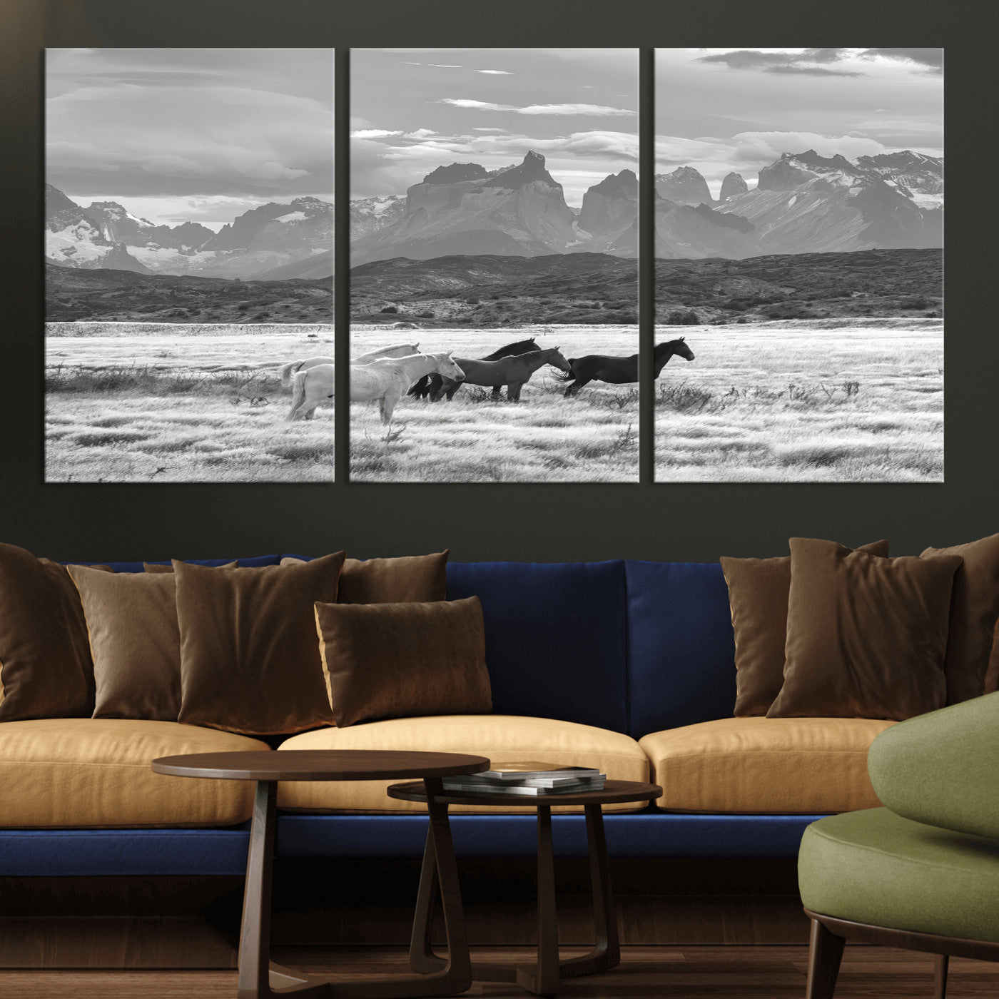 A black and white landscape of wild horses grazing in a vast grassland with towering mountains in the background, creating a moody and rustic western aesthetic.
