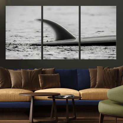 A black and white close-up of a surfboard fin resting on the sandy shore, highlighting minimalist beach aesthetics and classic surf culture.