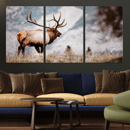Majestic elk with large antlers standing in grass with snowy mountains in background, perfect for rustic cabin or lodge style decor.