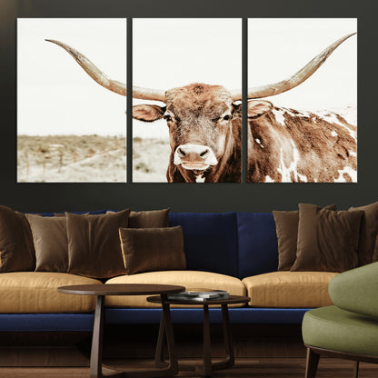A Texas longhorn bull with wide horns, standing in a dry field under soft light, ideal for rustic farmhouse or western-themed interiors.