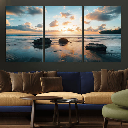 A serene beach at sunset with vibrant clouds, calm water, and rocks in the foreground reflecting the warm colors of the setting sun.