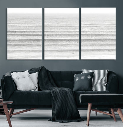 Monochrome photo of a lone surfer in calm layered waves, perfect for minimalist coastal or moody ocean-inspired wall decoration.