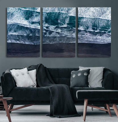 Canvas of aerial ocean waves crashing onto a black sand beach in moody tones, ideal for modern coastal or minimalist home decor.