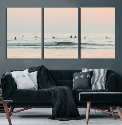 Dreamy photo of surfers waiting on soft pastel waves under a pink sunset sky, ideal for soft coastal minimalist or serene ocean-themed home decor.