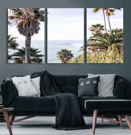 Scenic coastal view with tall palm trees overlooking a calm ocean, soft blue waves, and surfers in the distance, creating a peaceful tropical vibe.