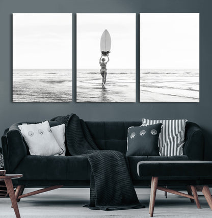 Black and white image of a female surfer holding a surfboard above her head while walking toward the ocean, creating a minimalist and bold coastal aesthetic.