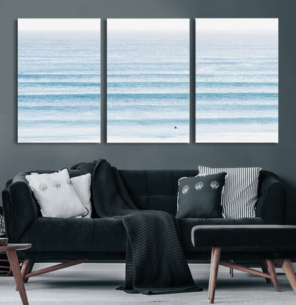 Minimalist ocean view with soft blue waves and a lone surfer, creating a serene and airy coastal aesthetic, perfect for tranquil home decor.