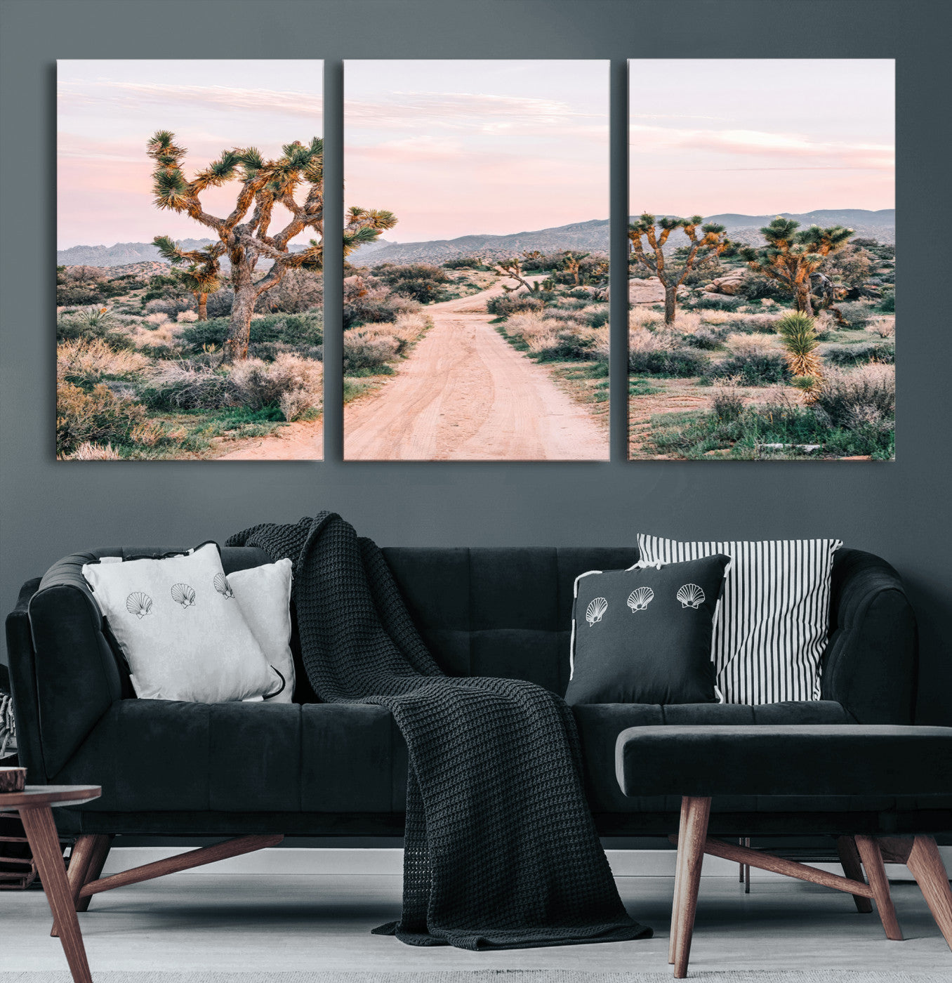 A dusty road winding through Joshua Tree National Park, framed by iconic twisted trees and warm desert tones under a soft pastel sky.