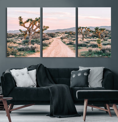 A dusty road winding through Joshua Tree National Park, framed by iconic twisted trees and warm desert tones under a soft pastel sky.