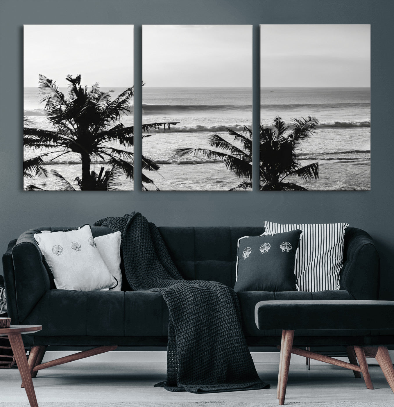 Black and white view of ocean waves crashing on a tropical coastline, framed by silhouetted palm trees under a vast, open sky.