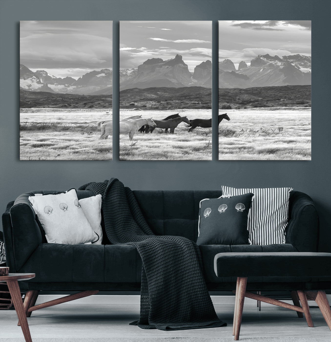A black and white landscape of wild horses grazing in a vast grassland with towering mountains in the background, creating a moody and rustic western aesthetic.