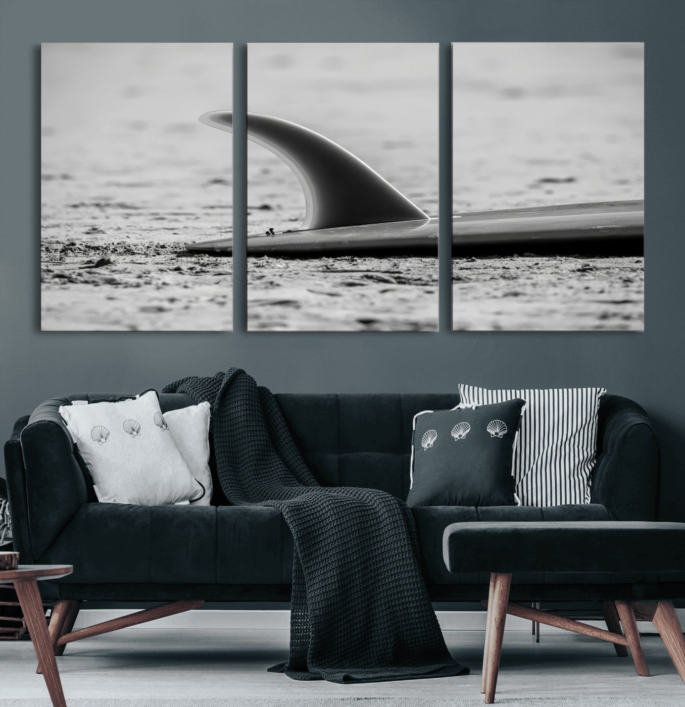 A black and white close-up of a surfboard fin resting on the sandy shore, highlighting minimalist beach aesthetics and classic surf culture.