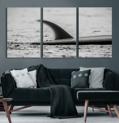A black and white close-up of a surfboard fin resting on the sandy shore, highlighting minimalist beach aesthetics and classic surf culture.