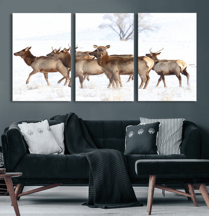 A group of elk standing on snowy terrain with a tree in the background, perfect for rustic or lodge-style winter wall decor.