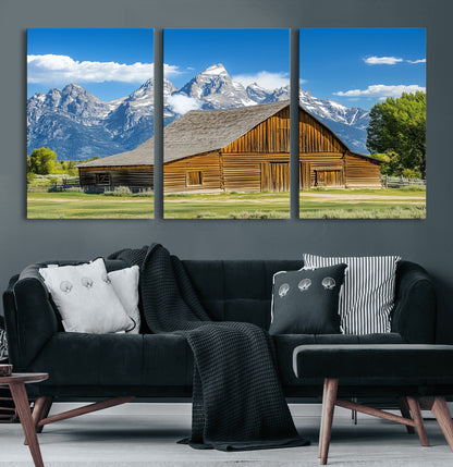 A rustic wooden barn sits in front of towering mountain peaks under a clear blue sky, perfect for farmhouse or cabin style interiors.