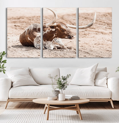 Texas Longhorn bull resting on dusty ground with warm tones, ideal for rustic western or farmhouse-themed wall decor.
