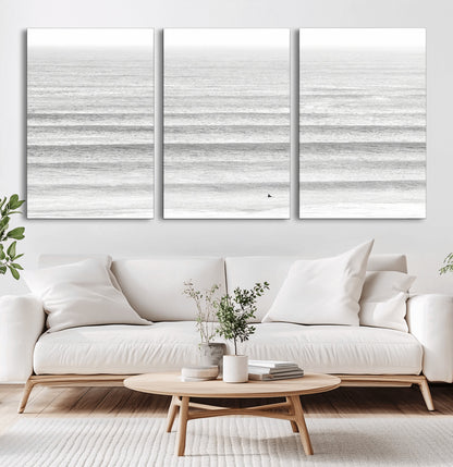 Monochrome photo of a lone surfer in calm layered waves, perfect for minimalist coastal or moody ocean-inspired wall decoration.