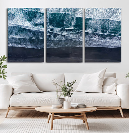 Canvas of aerial ocean waves crashing onto a black sand beach in moody tones, ideal for modern coastal or minimalist home decor.