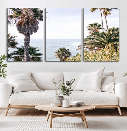 Scenic coastal view with tall palm trees overlooking a calm ocean, soft blue waves, and surfers in the distance, creating a peaceful tropical vibe.