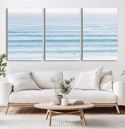 Minimalist ocean view with soft blue waves and a lone surfer, creating a serene and airy coastal aesthetic, perfect for tranquil home decor.