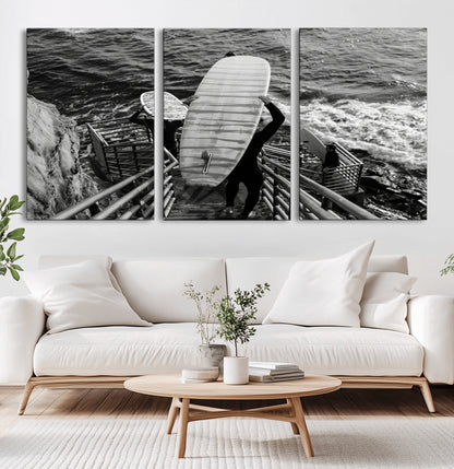 Black and white photo of surfers carrying boards down a rugged cliffside stairway, capturing a bold and adventurous coastal scene.