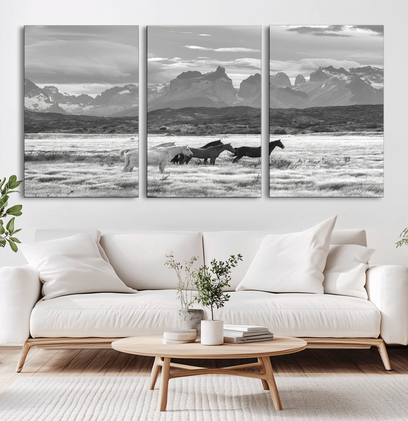 A black and white landscape of wild horses grazing in a vast grassland with towering mountains in the background, creating a moody and rustic western aesthetic.