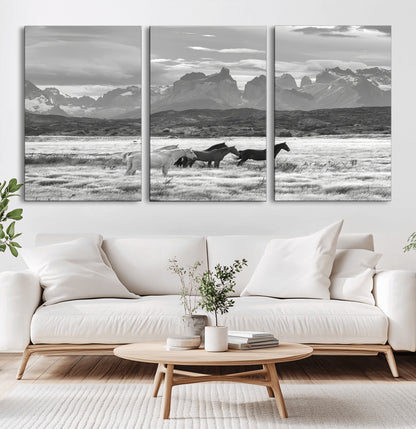 A black and white landscape of wild horses grazing in a vast grassland with towering mountains in the background, creating a moody and rustic western aesthetic.