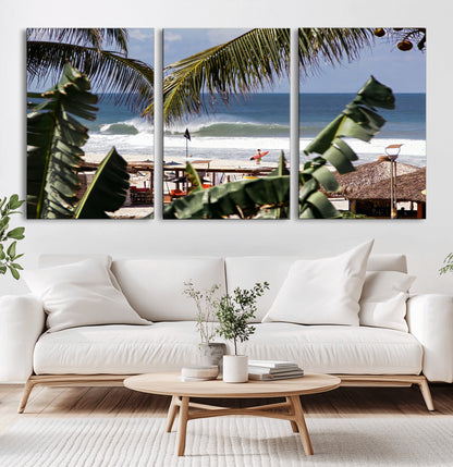 Canvas wall art of a tropical surf scene framed by palm trees, with a surfer on the shore and waves rolling in, ideal for beach-themed decor.
