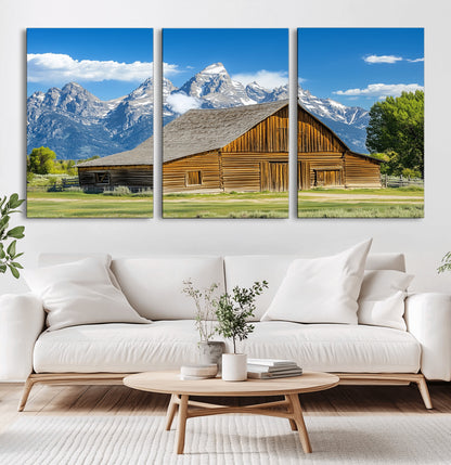 A rustic wooden barn sits in front of towering mountain peaks under a clear blue sky, perfect for farmhouse or cabin style interiors.